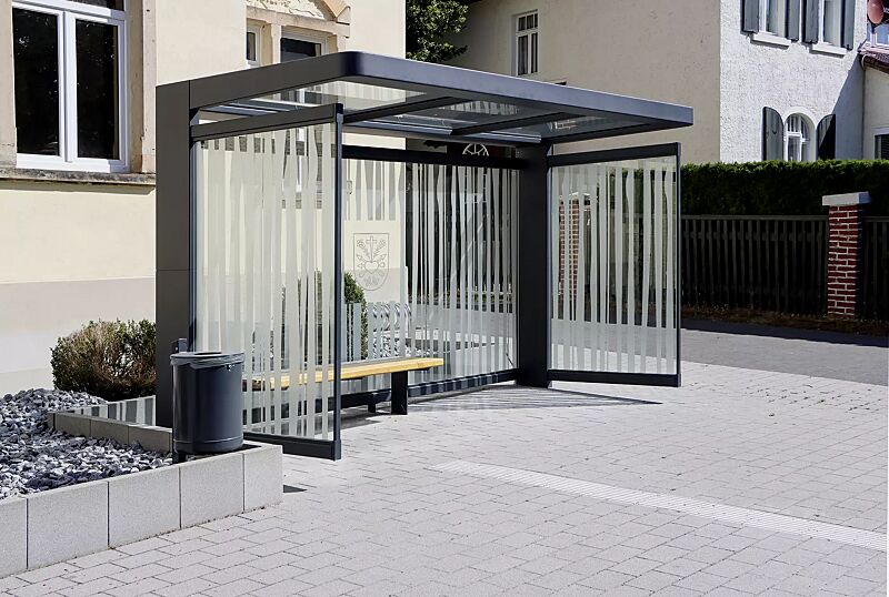 wartehalle-pure__shoKAT0071062 Wartehalle PURE, Dachbreite x Dachtiefe 4000 mm x 1800 mm, Rück- / Seitenwände ESG, Klarglas mit bauseitiger Folierung, Sitzbank PURE, Abfallbehälter KÖLN, Stahlkonstruktion in RAL 7016 anthrazitgrau