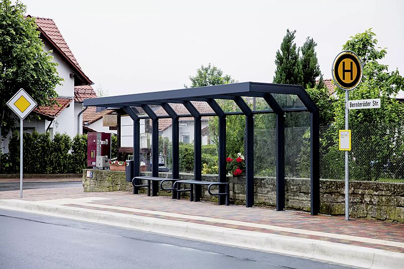 Wartehalle SATURN, auftragsbezogene Anpassung der Dachbreite x Dachtiefe 7060 mm x 1600 mm, inkl. Rückwände ESG, Klarglas, Sitzbänke SESTO und Abfallbehälter HALIFAX, Stahlkonstruktion in RAL 7016 anthrazitgrau