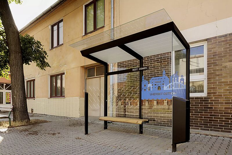 wartehalle-traxo__shoKAT0073434 Wartehalle TRAXO, Dachbreite x Dachtiefe 2800 mm x 1740 mm, Rück- / Seitenwände ESG, Klarglas, mit bauseitiger Beklebung sowie Abfallsammler (auftragsbezogen), Sitzbank Thermoholz Esche, Stahlkonstruktion in RAL 9005 tiefschwarz