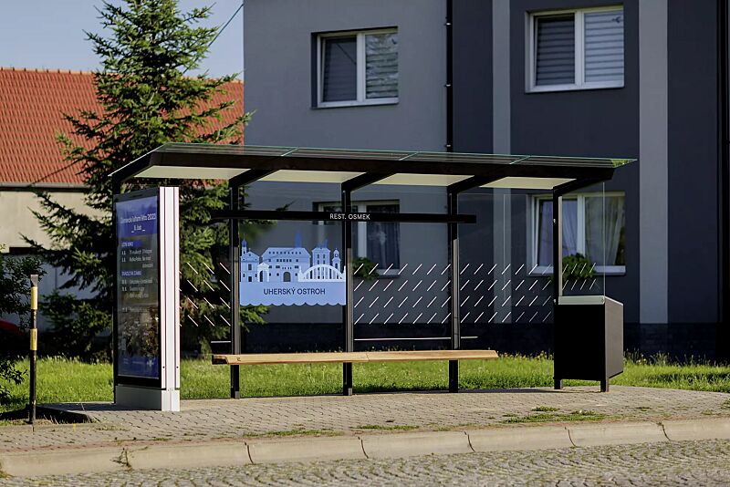 wartehalle-traxo__shoKAT0073436 Wartehalle TRAXO, Dachbreite x Dachtiefe 5560 mm x 1740 mm, Rück- / Seitenwand ESG, Klarglas, mit Siebdruckdekor und bauseitiger Beklebung sowie Werbevitrine, Abfallsammler (auftragsbezogen), Sitzbank Thermoholz Esche, Stahlkonstruktion in RAL 9005 tie...